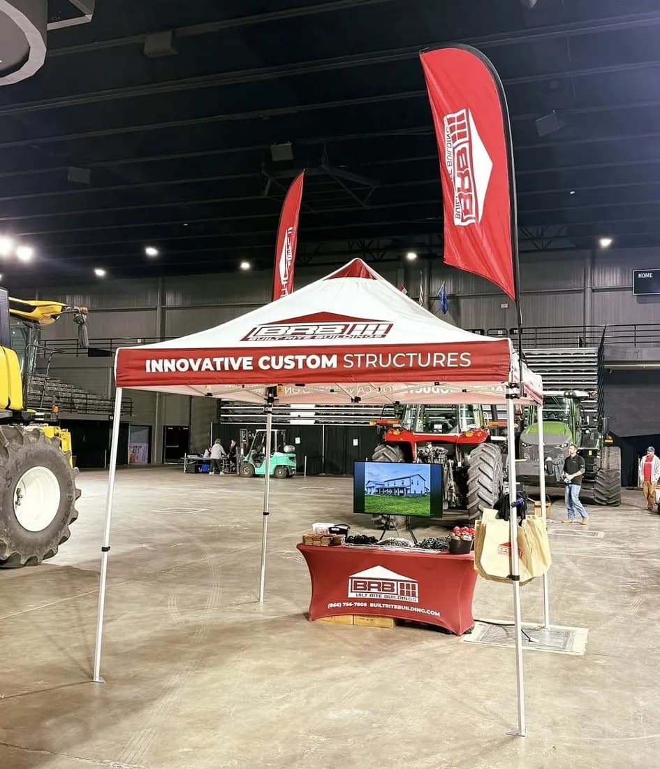 Built Rite Buildings custom canopy tent with feather flags and a fitted table cover at an indoor expo