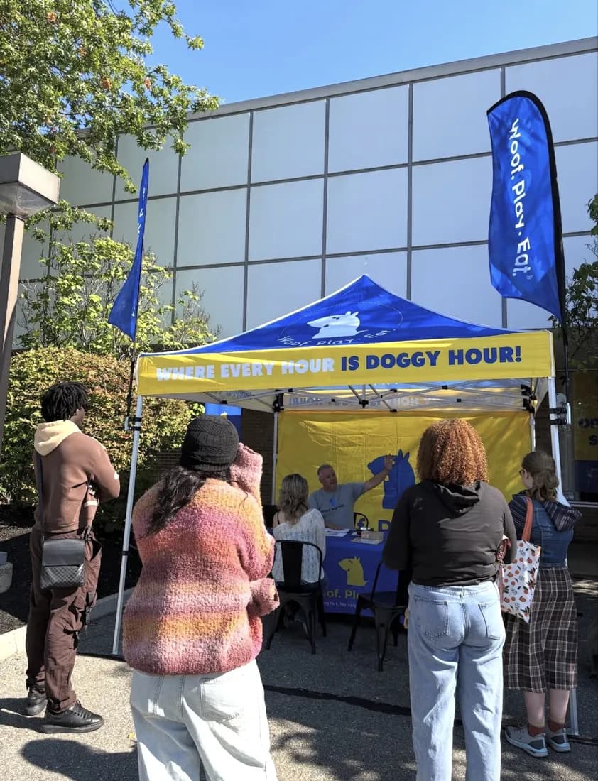 Visitors at a Woof. Play. Eat. canopy tent with feather flags and a backwall